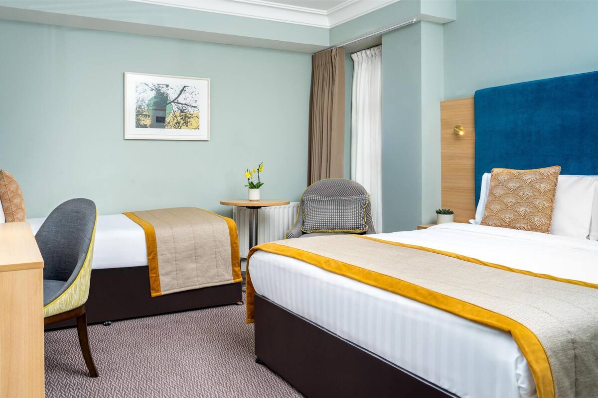 Una habitación de hotel con cama, escritorio, silla y una mesita con una planta.