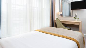 A hotel room with a bed, a desk, a chair, a television, and a window with curtains.