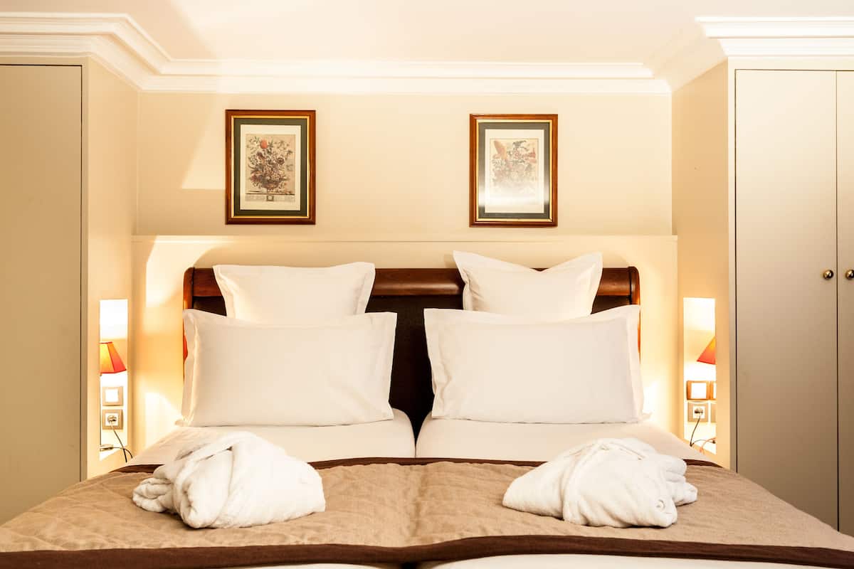 Une chambre d’hôtel avec un grand lit, deux tableaux encadrés au mur et un peignoir posé sur le lit.
