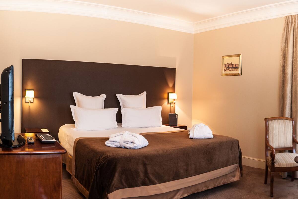 Une chambre d’hôtel avec un grand lit, un bureau avec une chaise, une télévision et un vase rempli de fleurs.