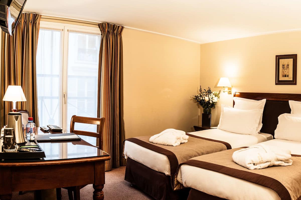 Une chambre d’hôtel avec deux lits, un bureau doté d’une machine à café, une chaise et une fenêtre avec des rideaux.