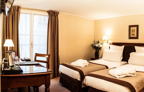 Habitación de hotel con dos camas, un escritorio con cafetera, una silla y una ventana con cortinas.