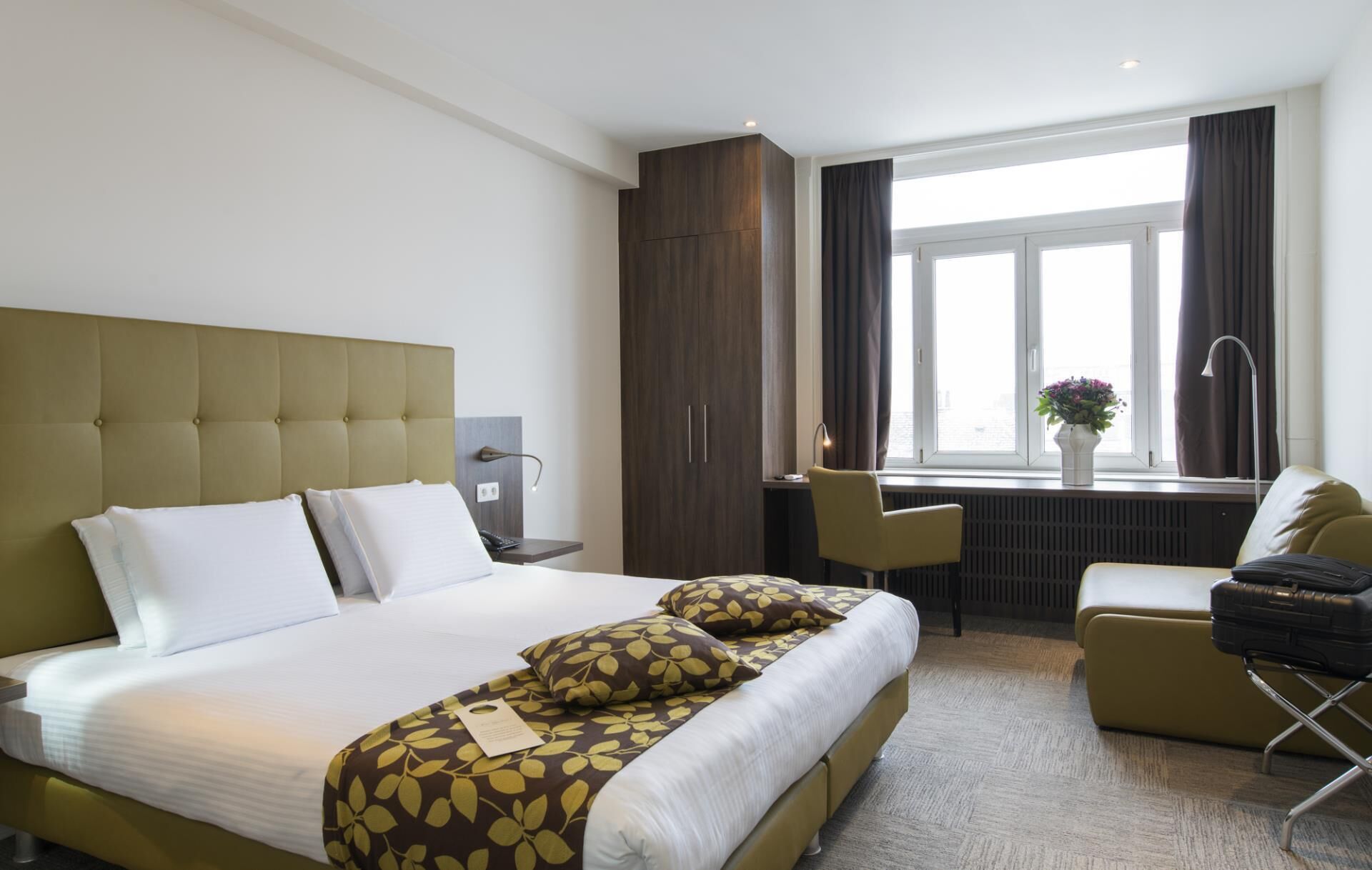 Habitación de hotel con una cama grande, un escritorio, una silla y una ventana con cortinas.