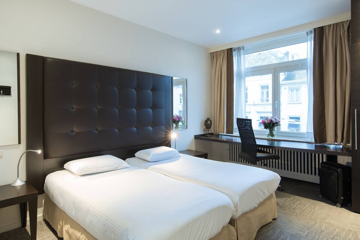 Habitación de hotel con dos camas, un ventanal con cortinas, un escritorio y una silla.