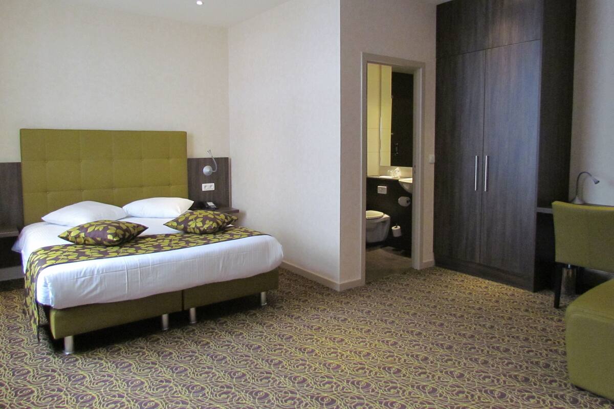Una habitación de hotel con una cama grande, un armario y un baño visible a través de una puerta abierta.