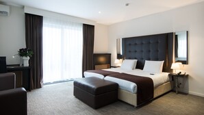 A modern hotel room with a large bed, a desk, a chair, and a window with curtains. - Hotel Chambord (Brussels)