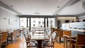 A spacious dining area with long tables and chairs, large windows, and a kitchen area visible in the background. - Hotel Chambord (Brussels)