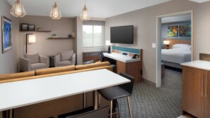 Une chambre d’hôtel comprenant un coin repas, une télévision, un lit et des œuvres d’art accrochées aux murs.