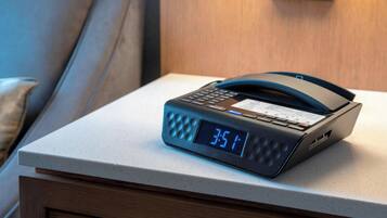A digital clock on a bedside table in a hotel room.