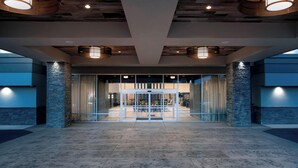 Un hall d’entrée spacieux au design moderne, doté d’une porte d’entrée en verre, de piliers en pierre et de luminaires suspendus.