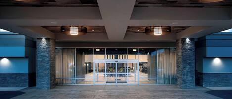 Un hall d’entrée spacieux au design moderne, doté d’une porte d’entrée en verre, de piliers en pierre et de luminaires suspendus.