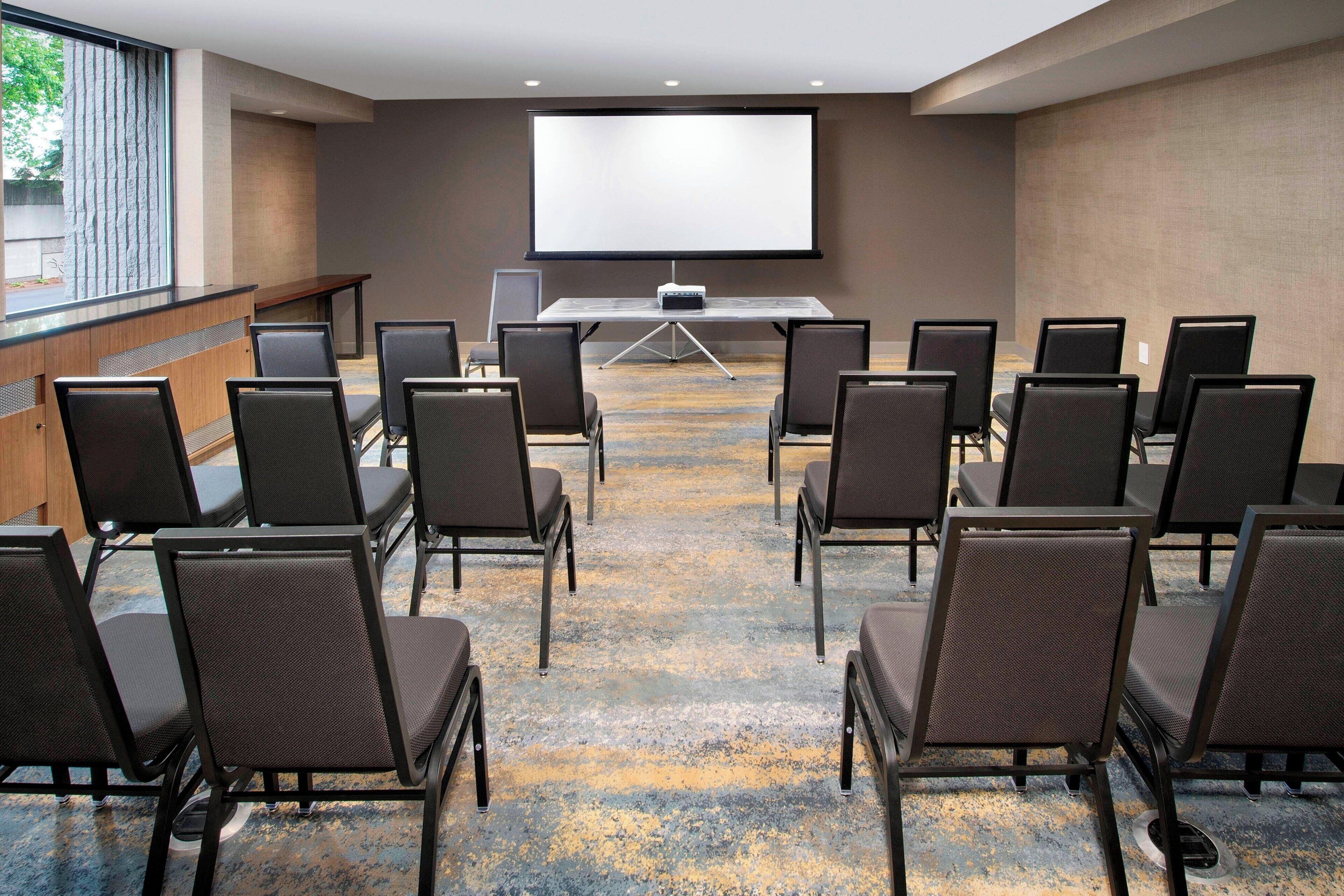 Un salón de conferencias con una pantalla grande, filas de sillas y suelo alfombrado.