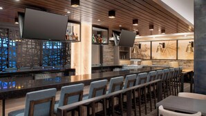 Un espace bar moderne doté d’un long comptoir, de nombreux sièges, notamment des tabourets et des tables, et d’un mur décoratif orné d’œuvres d’art abstraites.