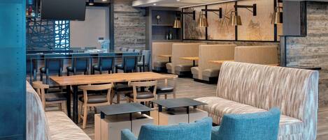 A modern lounge area with seating arrangements, a bar, and a flat-screen TV.
