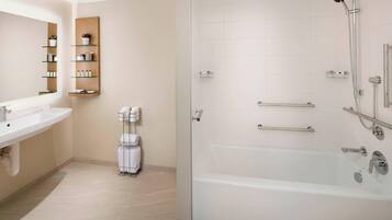 Un baño moderno con ducha de vidrio, lavamanos blanco y estante empotrado con artículos de aseo.