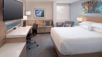 A hotel room with a large bed, a desk with a chair, a flat-screen TV, and artwork on the walls.