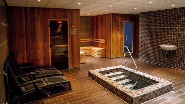 Un cuarto de sauna con paredes de madera, un banco, una bañera de hidromasaje y un lavamanos.