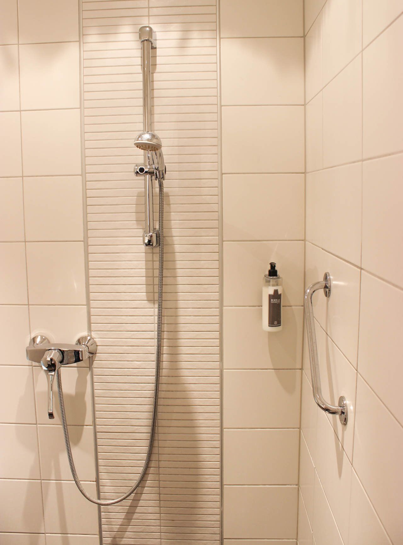 A shower with a handheld showerhead, a wall-mounted faucet, and a handheld shower hose.