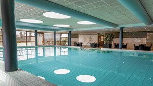 Una piscina interior con agua cristalina, suelo de baldosas y un área de descanso con sillas y mesas.