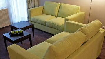 Een woonkamer met een gele bank, een bijpassende fauteuil en een kleine tafel met appels.