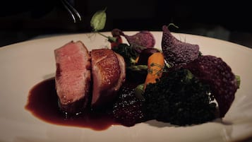 A plated dish with sliced meat, vegetables, and a dark sauce.
