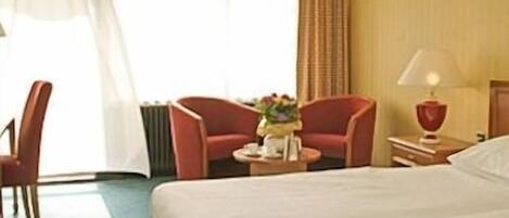 Une chambre d’hôtel avec un lit, un bureau avec une lampe, une chaise et une petite table sur laquelle se trouve une assiette de nourriture.