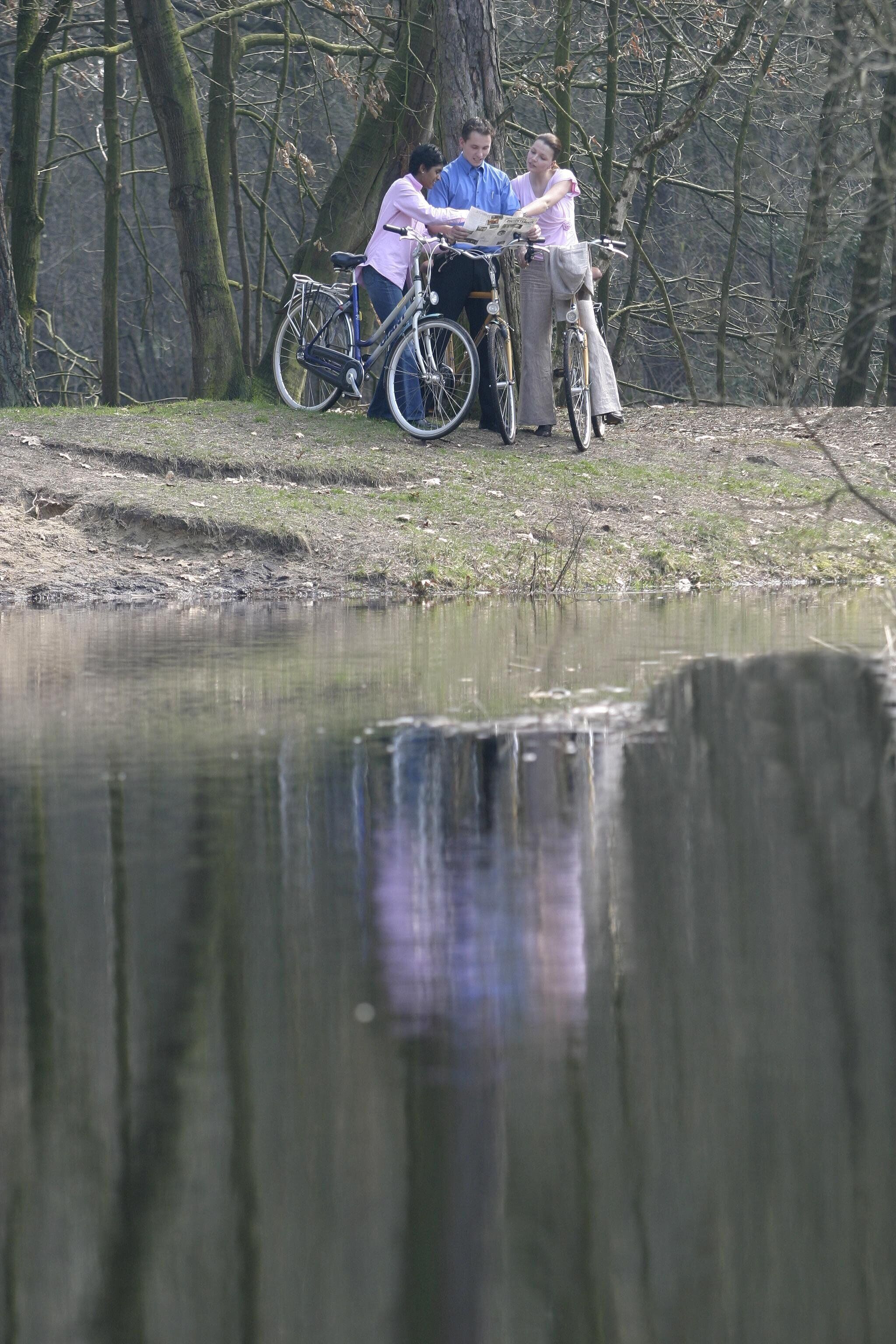 Un grupo de personas junto a bicicletas cerca de un cuerpo de agua en un área boscosa.