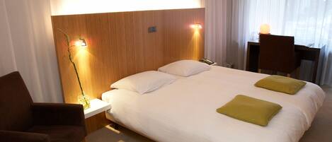 A hotel room with a large bed, two bedside lamps, a desk, and a chair.