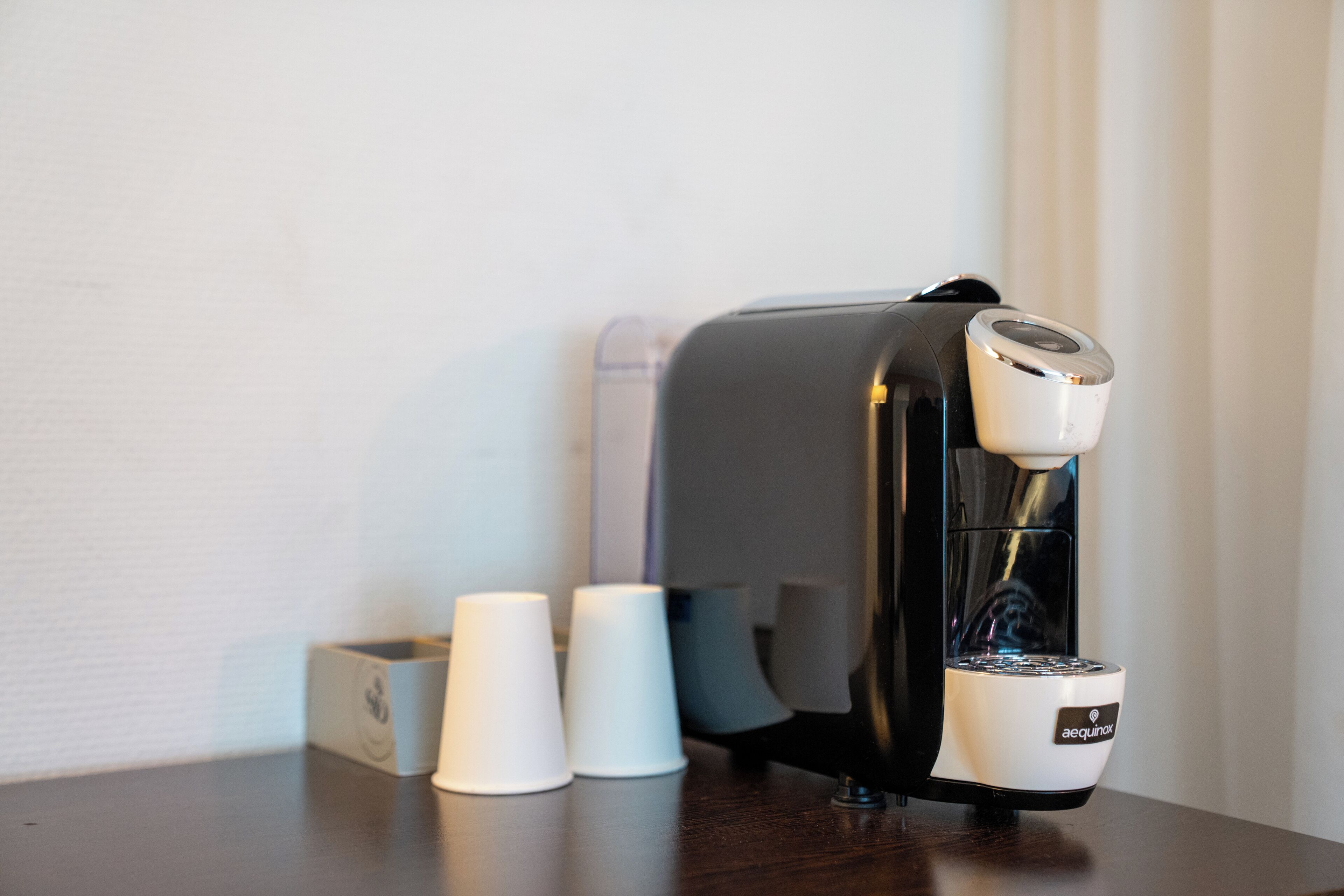 Une machine à café dotée d’un réservoir d’eau et d’un compartiment pour les capsules de café, le tout posé sur une surface en bois.