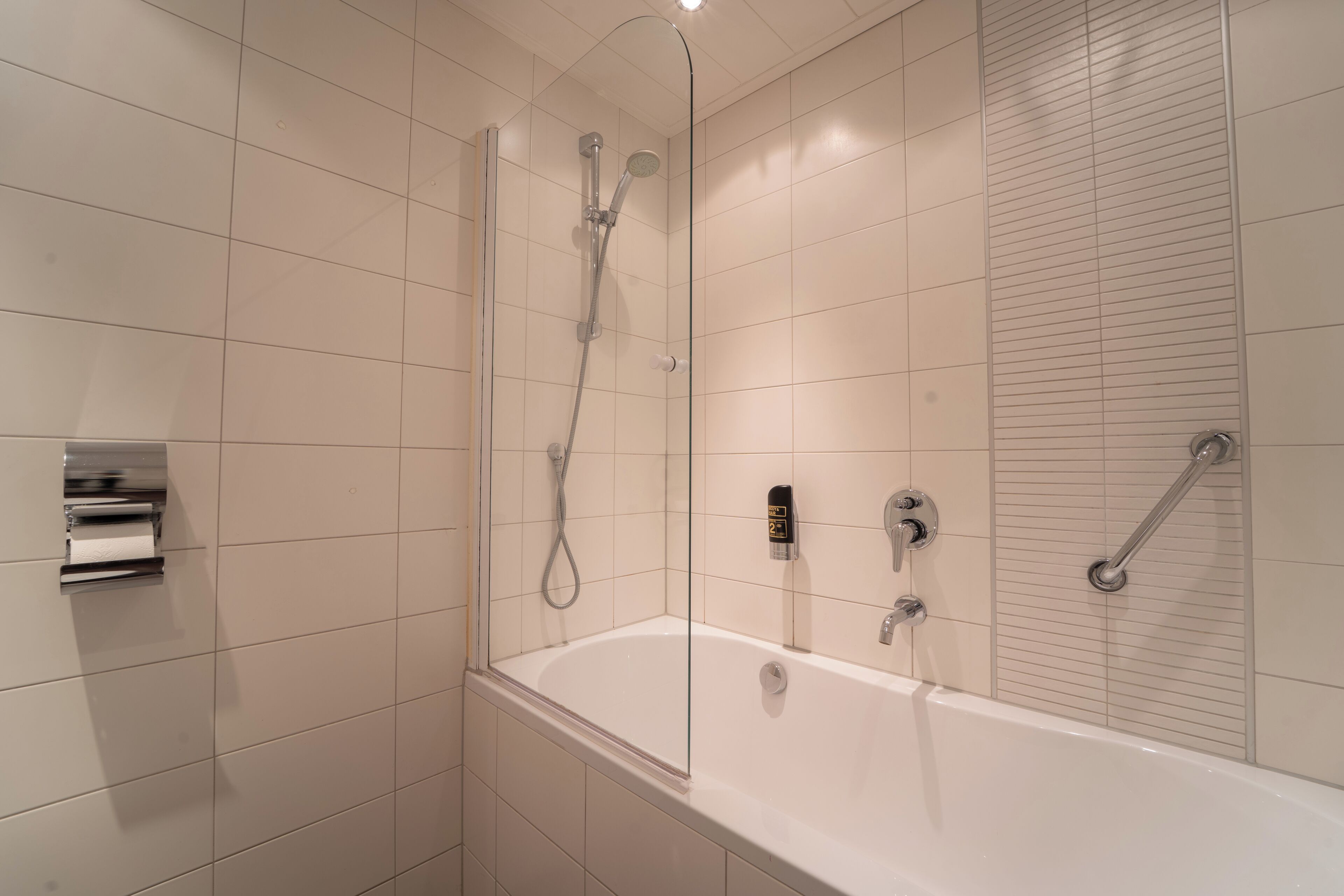 A modern bathroom with a glass-enclosed shower, a standalone bathtub, and a toilet with a paper towel dispenser.