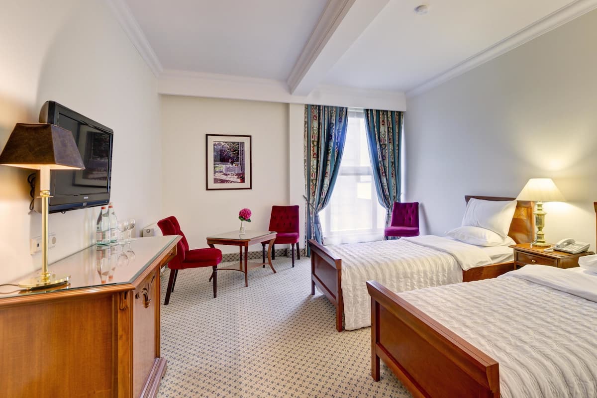 A hotel room with two beds, a desk, a TV, a chair, a table, and a window with curtains.