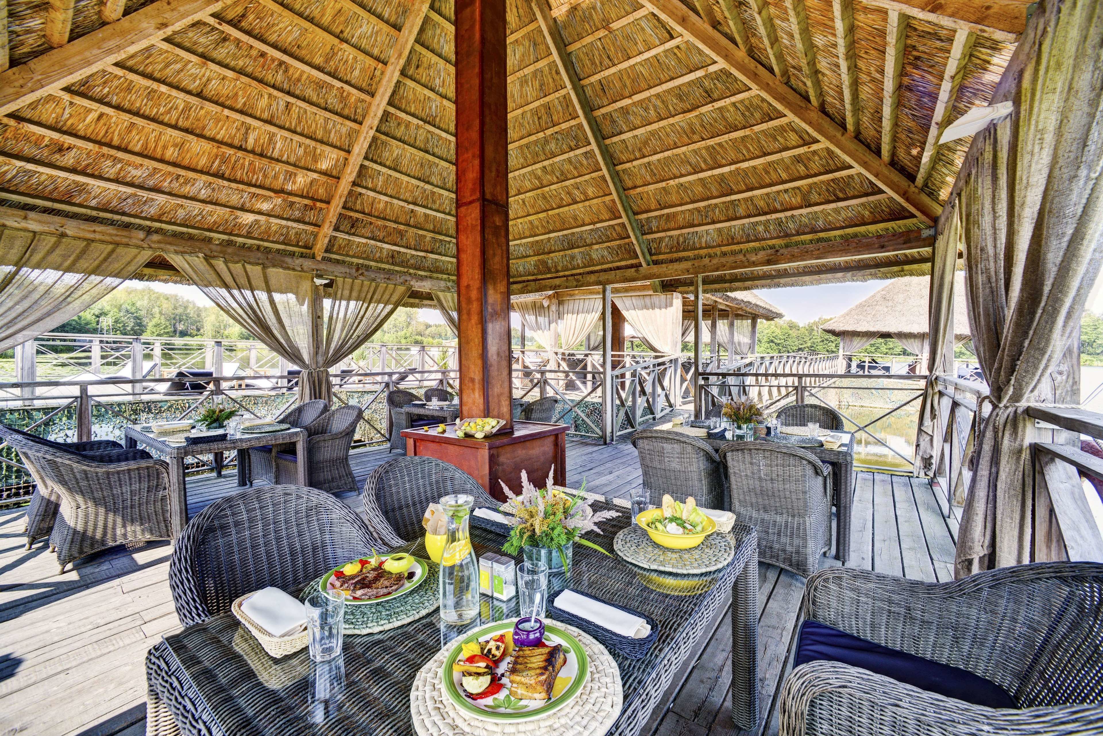 An outdoor dining area with wicker furniture, a thatched roof, and a view of the landscape.