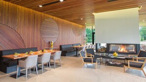 A modern dining area with a long wooden table, cushioned chairs, and a fireplace. - Vilnius Grand Resort (Kalikstiškes)