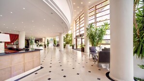 A spacious lobby with a reception desk, seating area, and large windows allowing natural light. - Vilnius Grand Resort (Kalikstiškes)