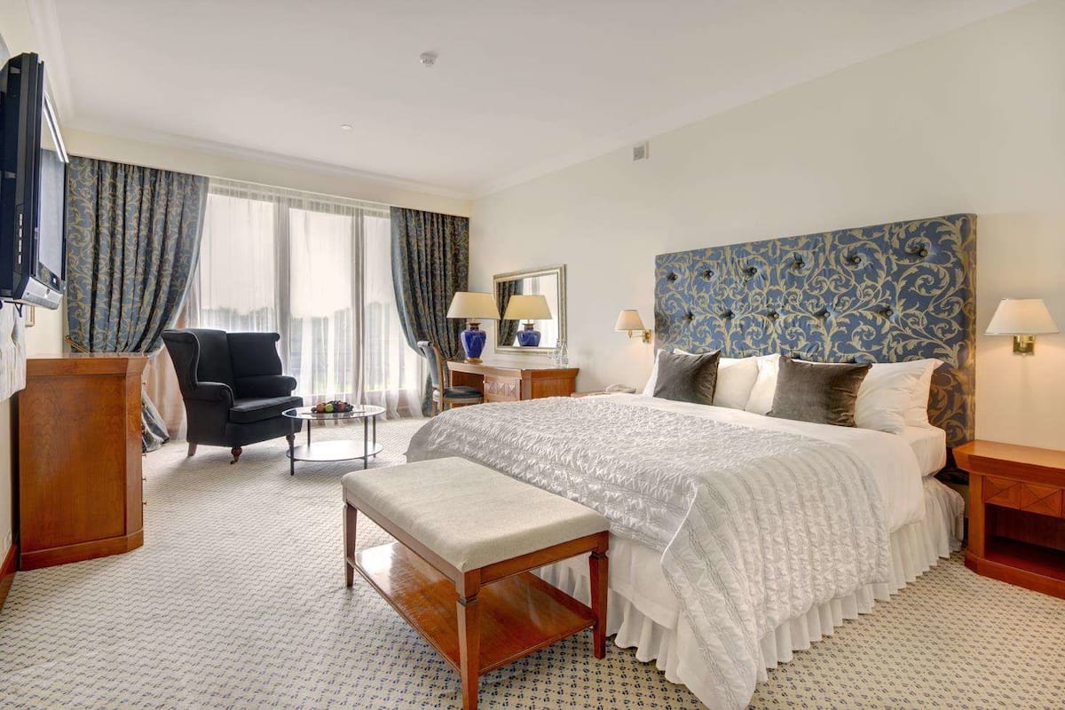 A hotel room with a large bed, a desk, a chair, and a bench.