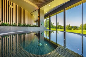 Una piscina interior moderna con un diseño de baldosas hexagonales, grandes ventanales que ofrecen vistas a un paisaje verde y un diseño de pared con listones de madera.