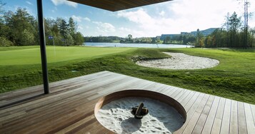 Una terraza de madera con un jacuzzi, un campo de golf y vistas a un lago.