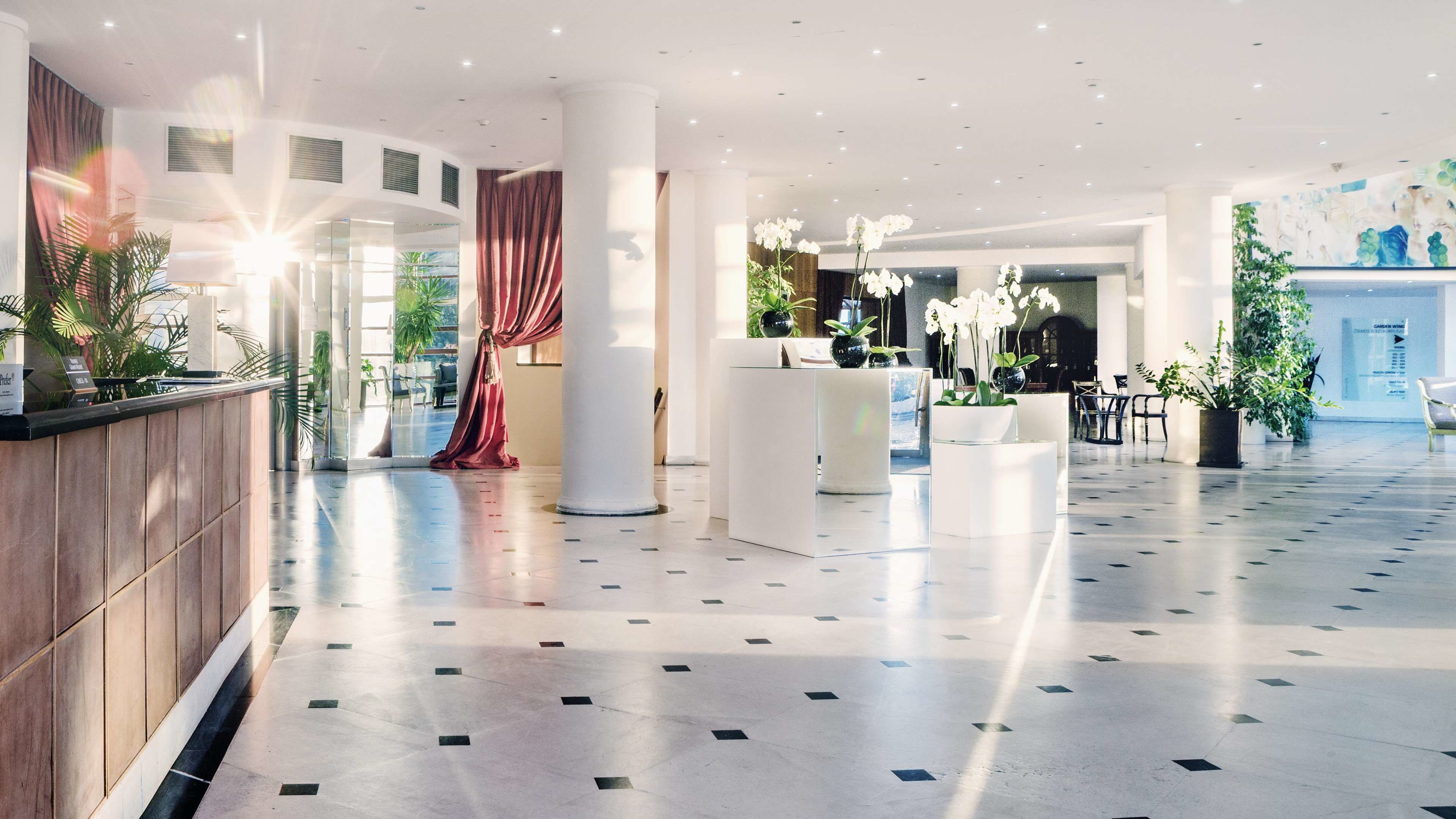 A spacious lobby with a tiled floor, a reception desk, and potted plants.