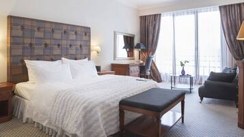 A hotel room with a large bed, a bedside table, a chair, a desk, and a window with curtains.