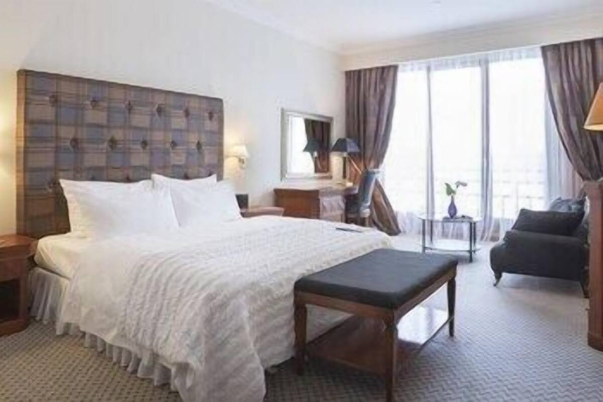 A hotel room with a large bed, a bedside table, a chair, and a view of the outdoors.
