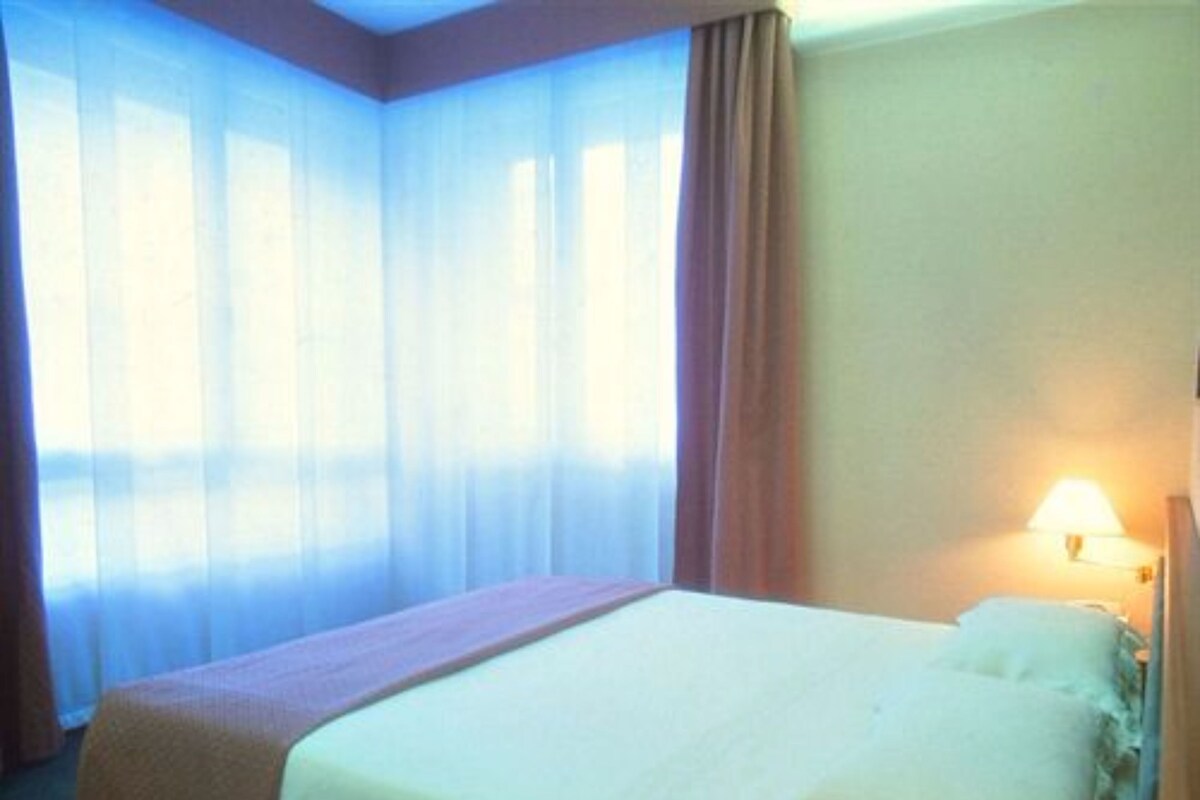 A hotel room with a bed, curtains, and a lamp.