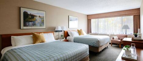 A hotel room with two beds, a desk, a chair, and a window with curtains.