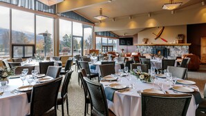 A restaurant with multiple dining tables set for guests, large windows offering a view of the outdoors, and a fireplace in the background. - Lobstick Lodge (Jasper)