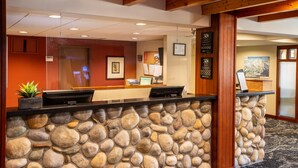 A reception desk with a stone wall, wooden beams, and framed pictures on the wall. - Lobstick Lodge (Jasper)