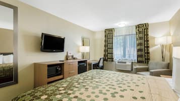 Ett hotellrum med en säng, ett skrivbord, en stol, en tv, en spegel, ett fönster med gardiner och en lampa.