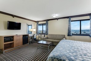 Hotellihuone, jossa on sänky, työpöytä tietokoneella, televisio, mikroaaltouuni, sohva ja näkymä kaupunkiin.