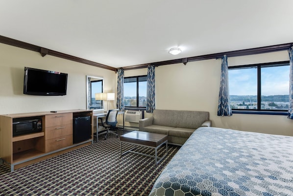 A hotel room with a bed, a desk with a computer, a TV, a microwave, a sofa, and a view of the city. - Econo Lodge Madison East (Madison)