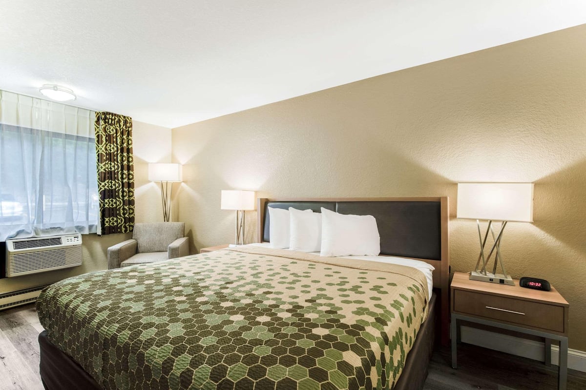 Una habitación de hotel con una cama, dos lámparas de noche, una silla, una mesita de noche y una ventana con cortinas.