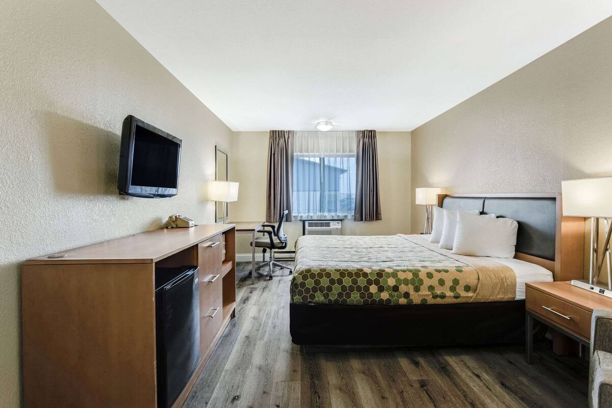 Ein Hotelzimmer mit Bett, Schreibtisch, Stuhl, Fernseher und einem Fenster mit Vorhängen.