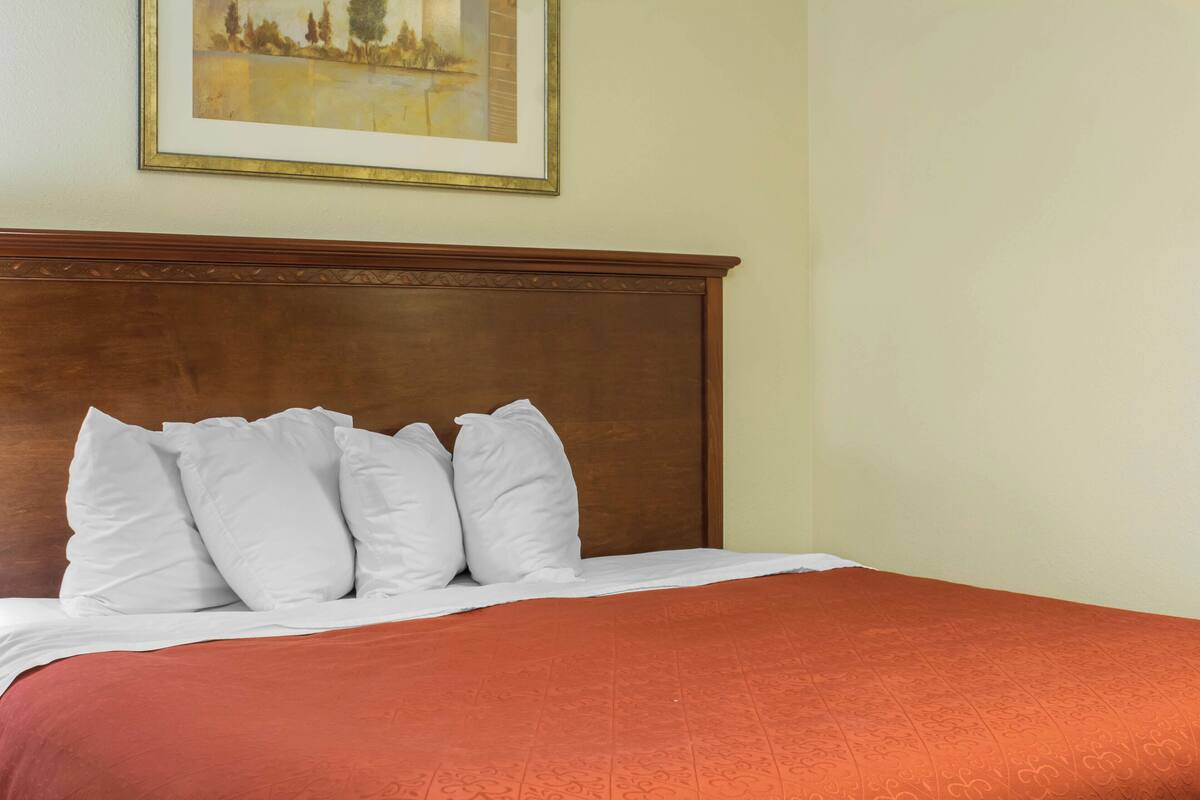A neatly made bed with white pillows and a red bedspread in a hotel room.